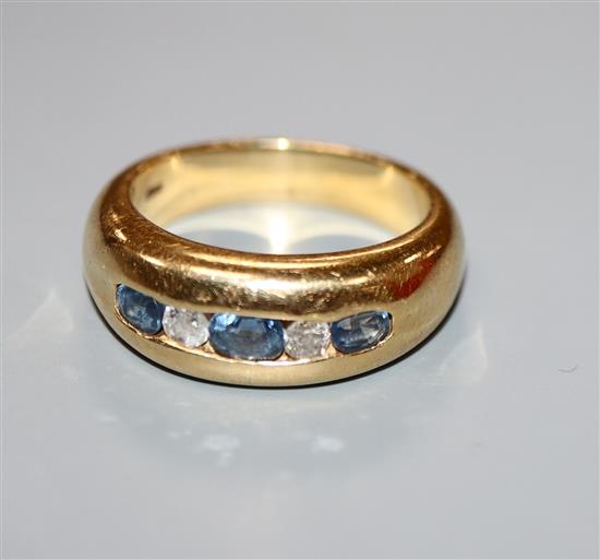 A modern yellow metal and channel set three stone oval cut sapphire and two round cut diamond set half hoop ring, size N/O.